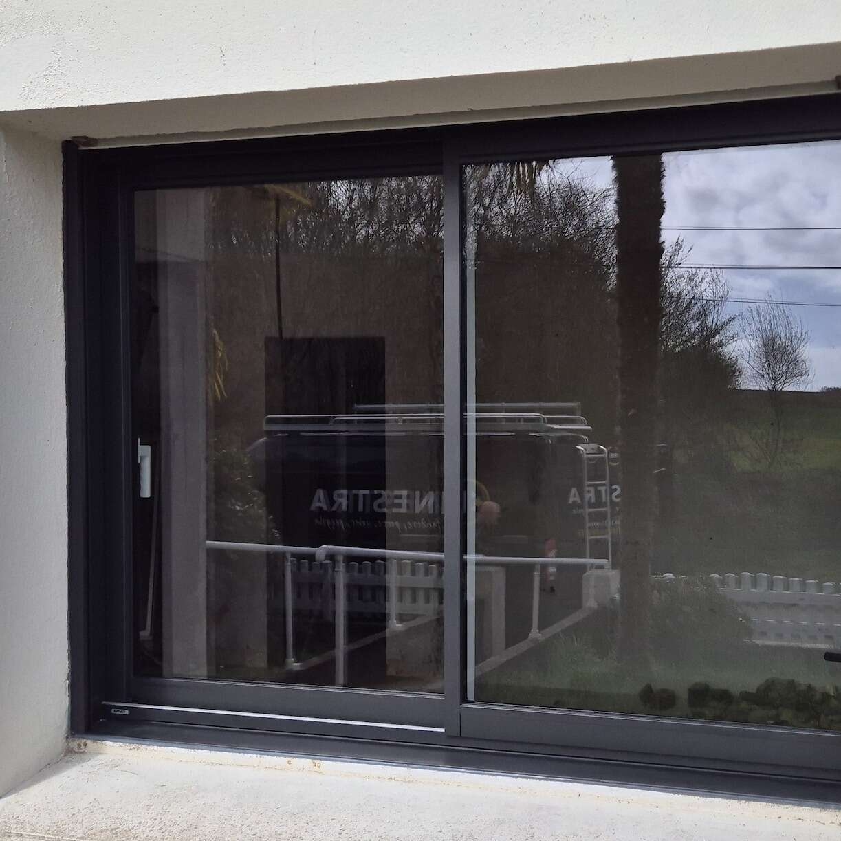 Baie coulissante en aluminium anthracite posée, avec l'utilitaire Finestra reflété dans le vitrage