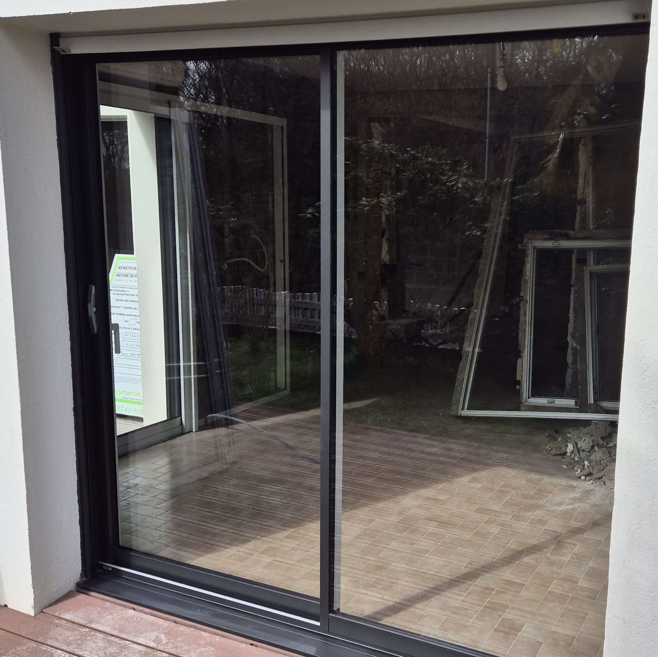 Baie coulissante aluminium noire neuve, les anciennes menuiseries déposées dans le jardin